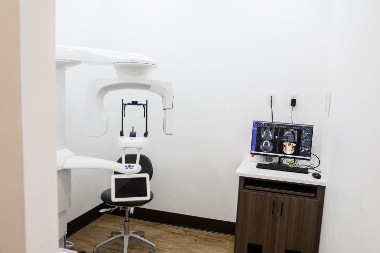 Dental imaging room with a panoramic X-ray machine and a computer showing scans.