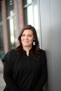 Portrait of Bry, an office manager, smiling indoors, appears to be a professional staff headshot.
