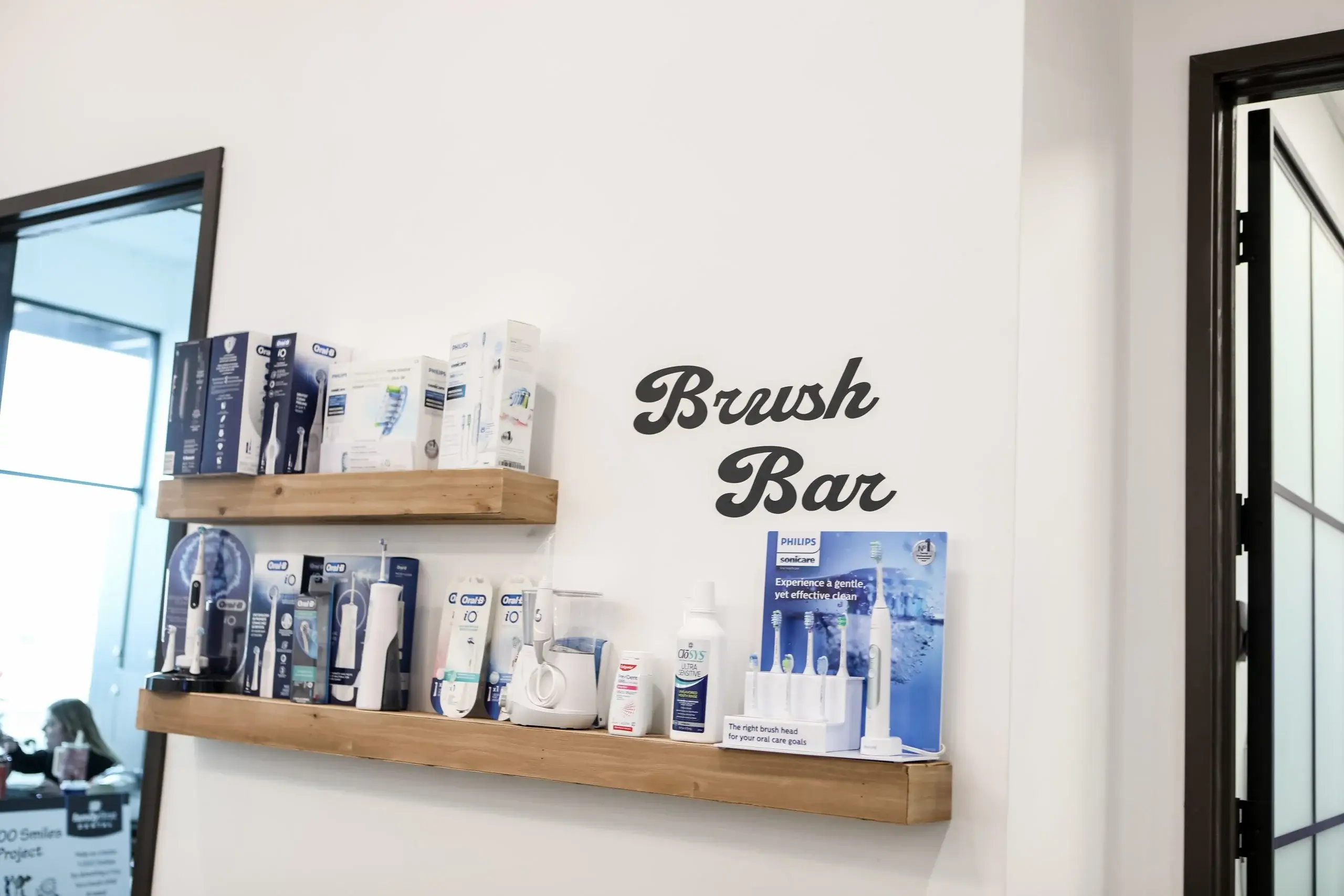 Family First Dental Brush Bar with electric toothbrushes and oral care products on wooden shelves.