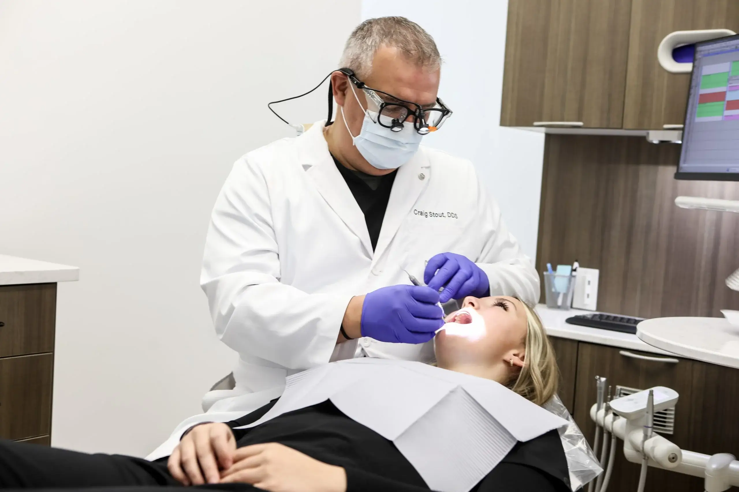 Family First Dental dentist in loupes and mask performing a dental exam on a patient.