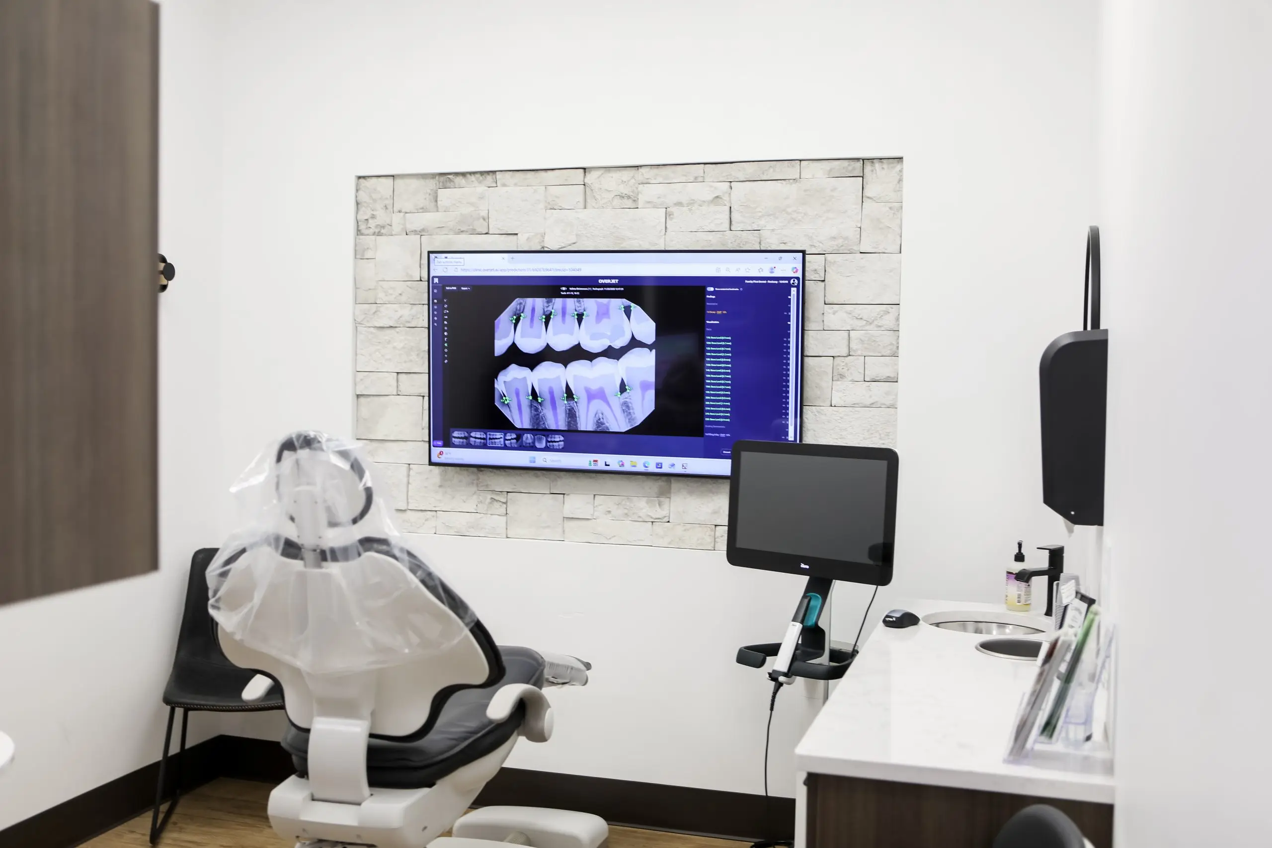 dental treatment room with a chair, wall screen showing dental scans, & digital imaging equipment