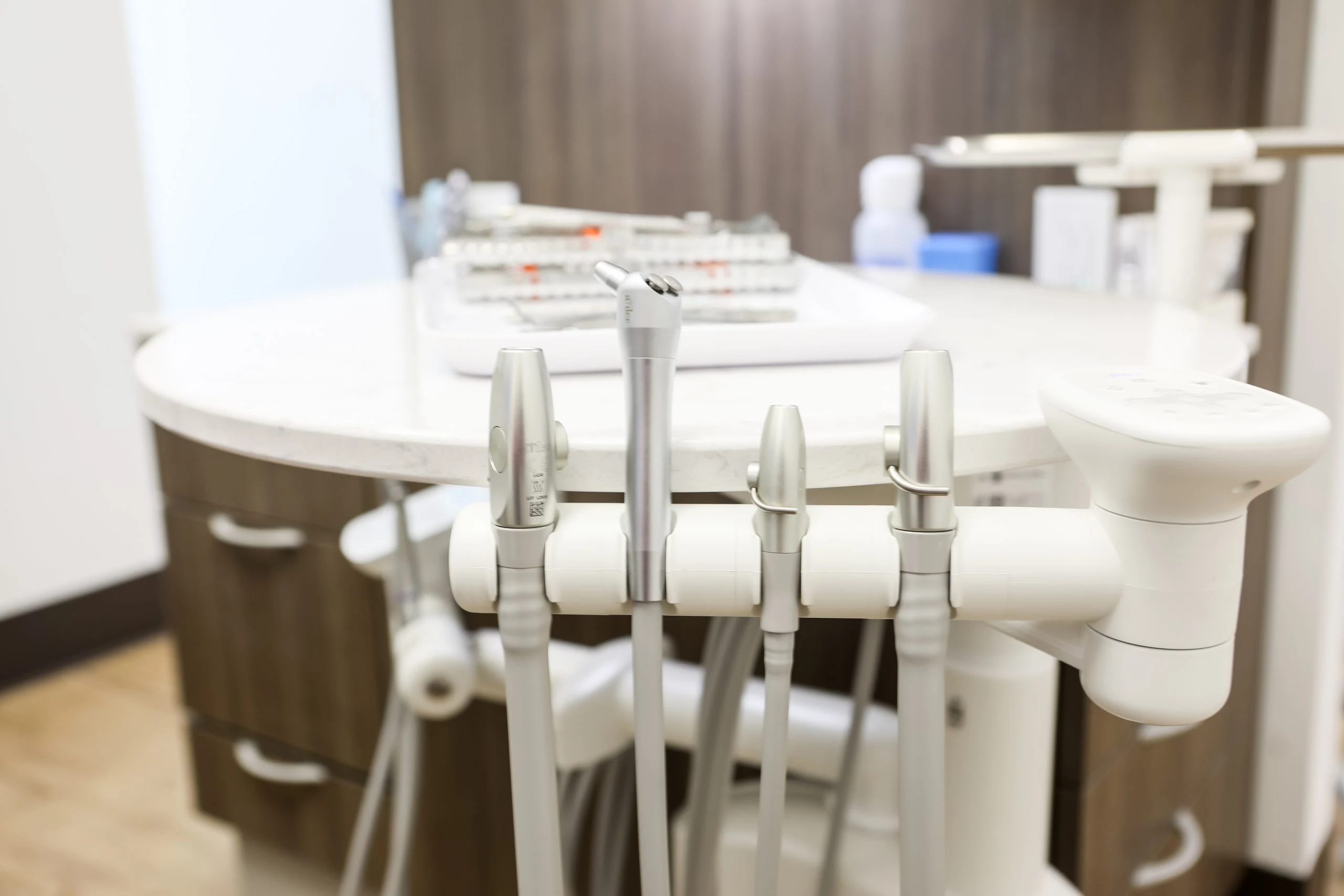 Close-up of dental handpieces and control unit beside a treatment chair in a clean surgery room.