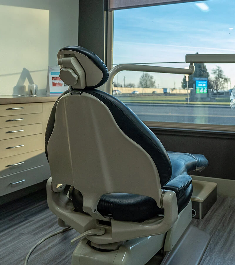 Empty dental treatment chair beside a large window in a clean surgery room